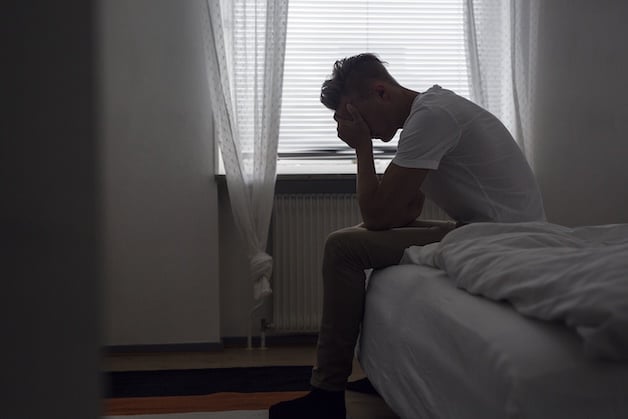young man upset sitting on end of bed.