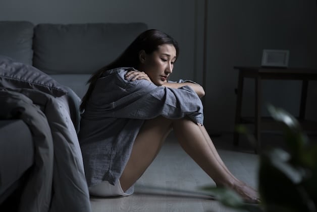depressed woman sitting on bedroom floor